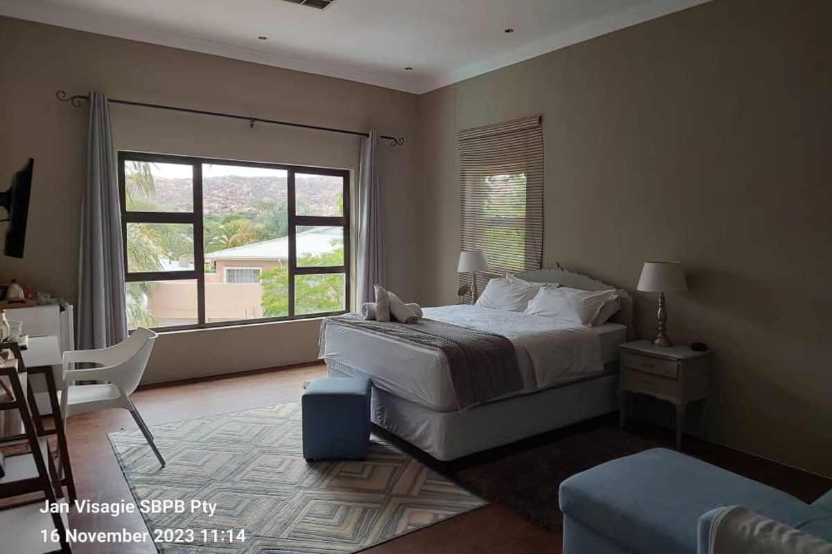 A spacious bedroom featuring large windows with scenic views, recessed ceiling lighting, and neutral wall tones.