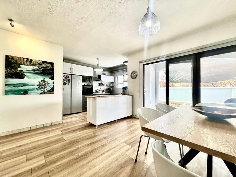Modern open-plan kitchen and dining area featuring sleek cabinetry, a central island, and large sliding doors providing seamless access to the outdoor patio.