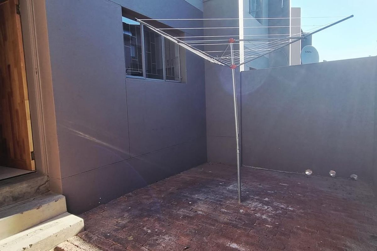 A private rear courtyard featuring brick paving, a wall-mounted security gate, and a fixed rotary clothesline, providing a functional outdoor utility space.