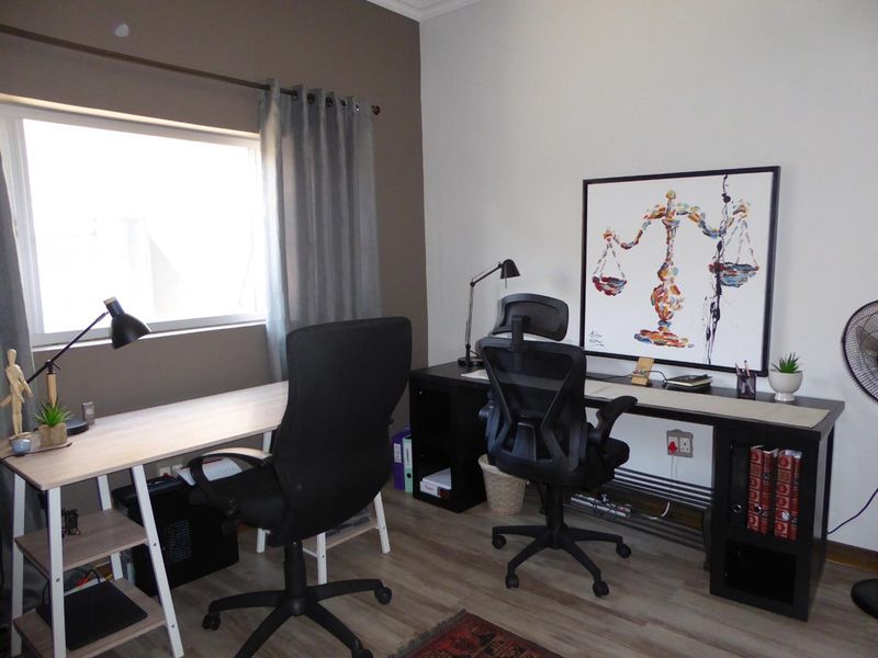 A functional home office space featuring laminate flooring, neutral wall tones, and a large window providing natural light.