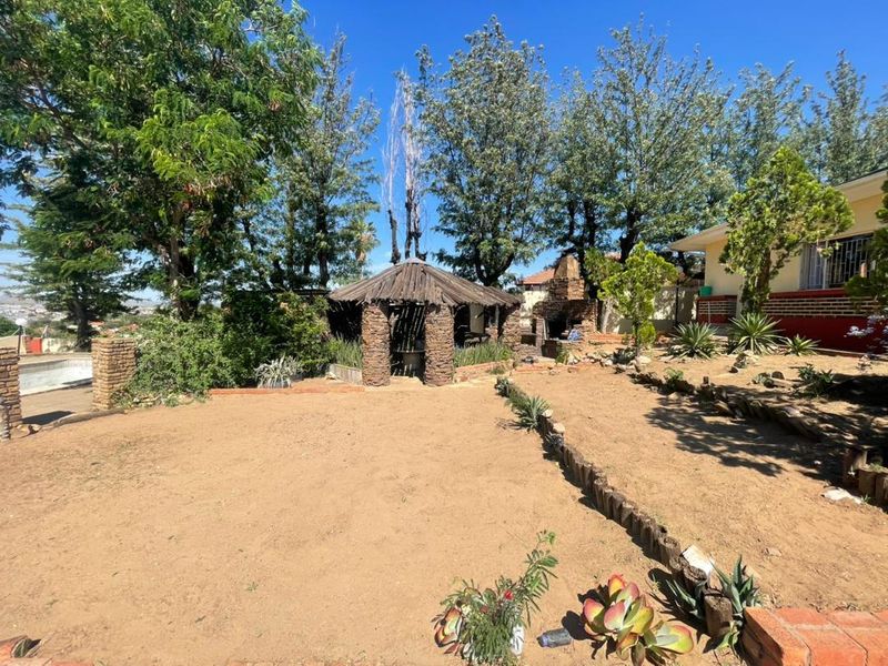 Spacious backyard featuring a rustic thatched gazebo, stone pillars, and an outdoor brick fireplace, offering potential for landscaping and outdoor entertainment development.