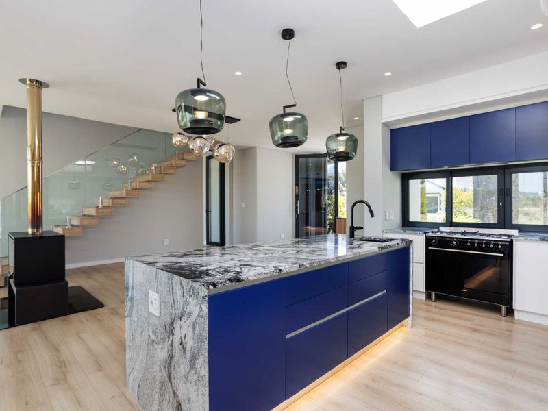 Modern open-plan kitchen and living area featuring a striking blue island, stone countertops, a wood-burning fireplace, and a contemporary floating staircase.