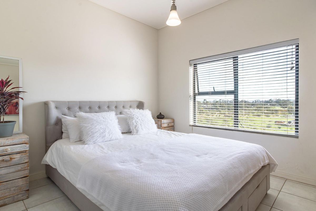A bright and well-maintained bedroom featuring tiled flooring, a large window with fitted blinds, and neutral wall finishes.