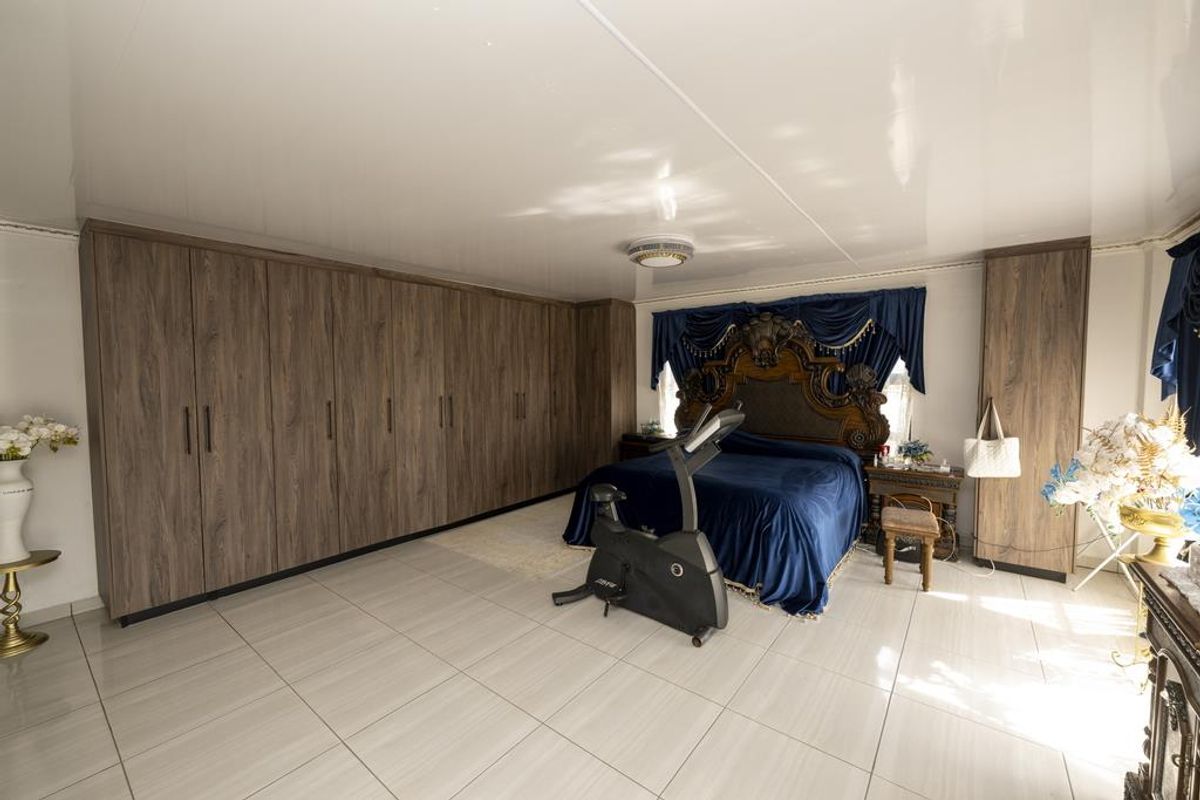 Spacious bedroom featuring extensive built-in wood-finish wardrobes, large format floor tiles, and a glossy ceiling finish.