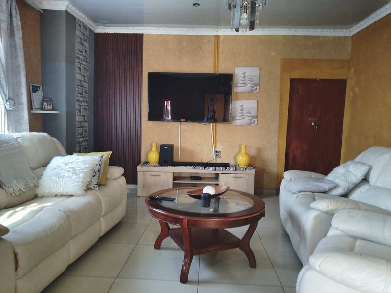 A living room featuring tiled flooring, crown molding, and a wall-mounted television with textured wall accents.