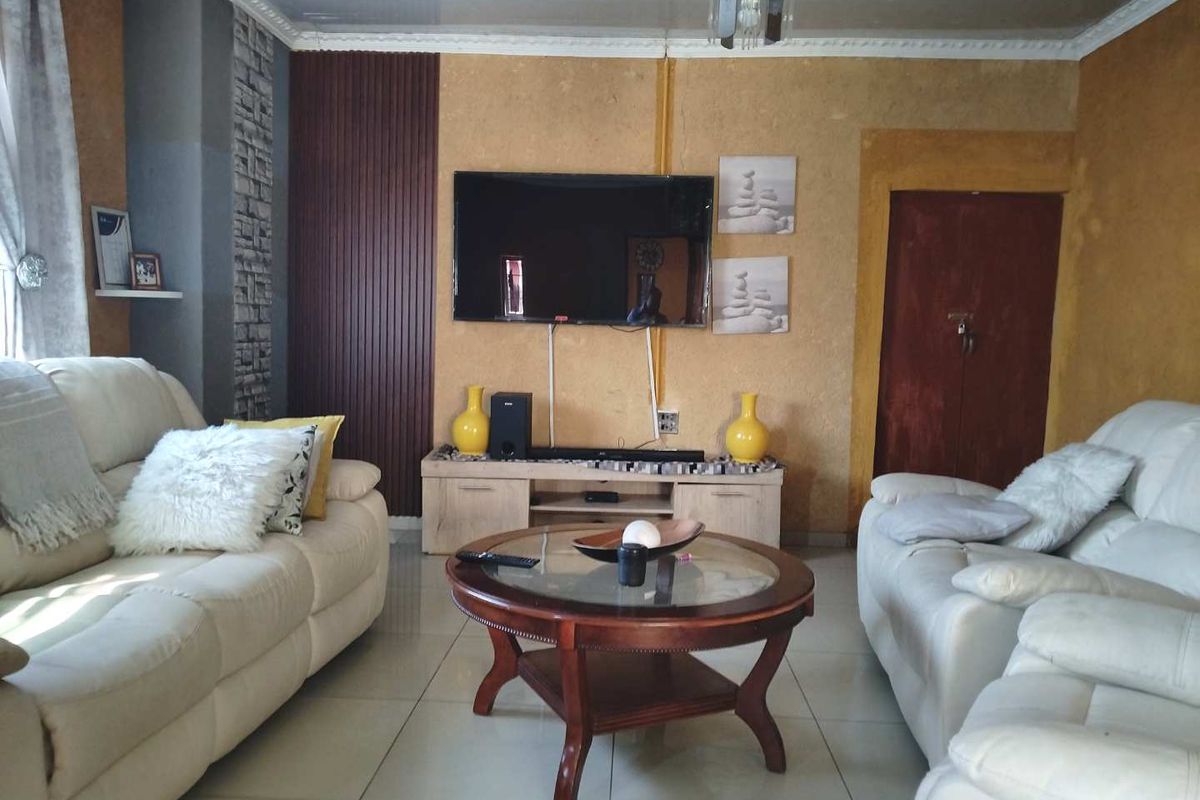 A living room featuring tiled flooring, crown molding, and a wall-mounted television with textured wall accents.