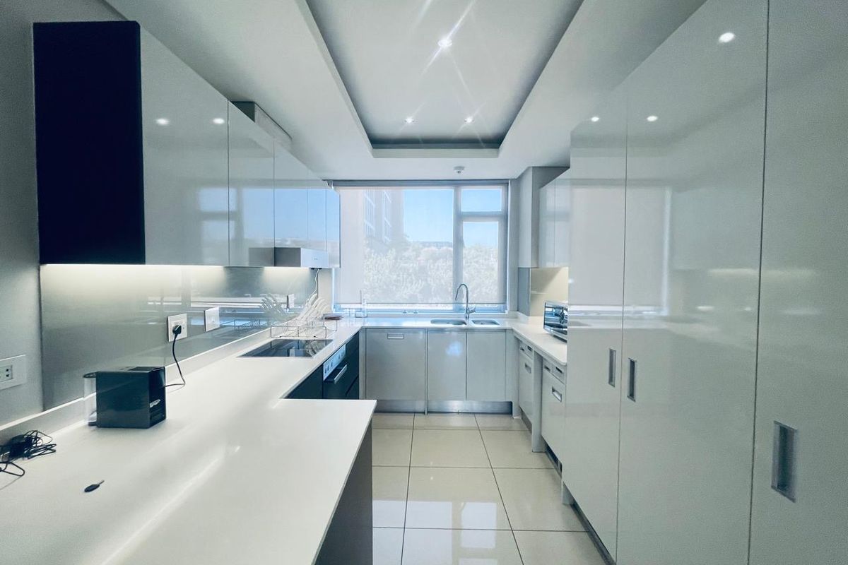 Modern galley-style kitchen featuring high-gloss white cabinetry, quartz countertops, integrated appliances, and sleek tiled flooring with ample natural light.
