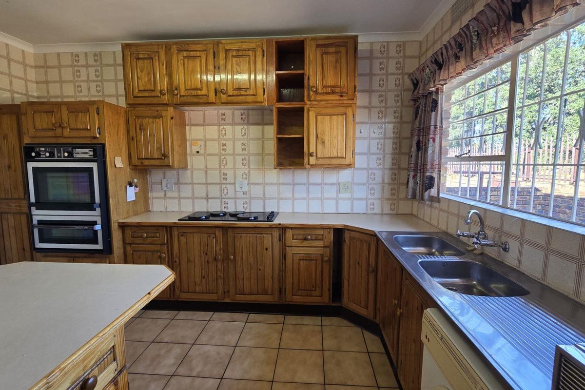 A dated kitchen featuring wooden cabinetry, a built-in oven, a hob, and a double stainless steel sink with tiled splashbacks.