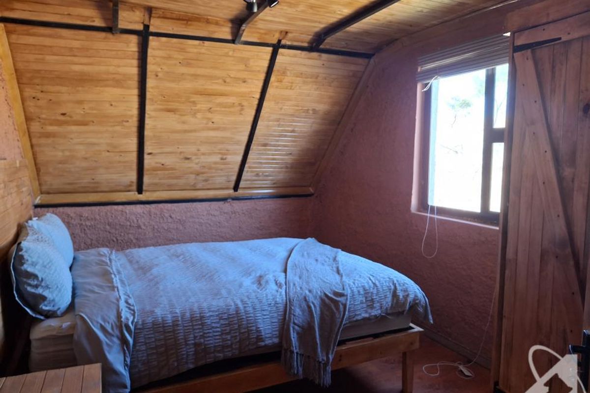 A cozy bedroom featuring a sloped timber-clad ceiling, textured walls, and a built-in wooden wardrobe.