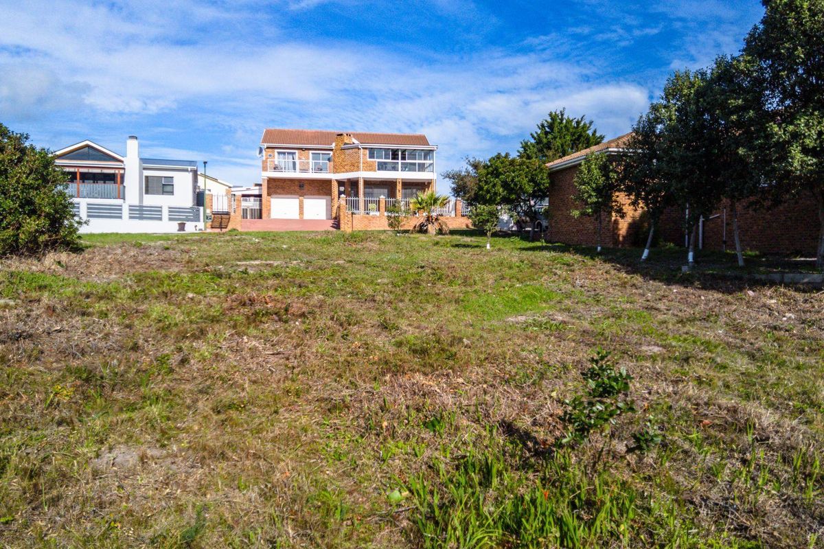 A vacant residential plot of land with natural grass coverage, offering a clear view of the neighboring brick-built residential properties.