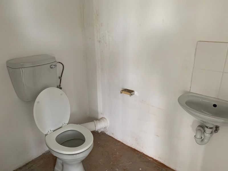 A basic, unfinished bathroom featuring a standard toilet and wall-mounted basin, requiring cosmetic updates and floor finishing.
