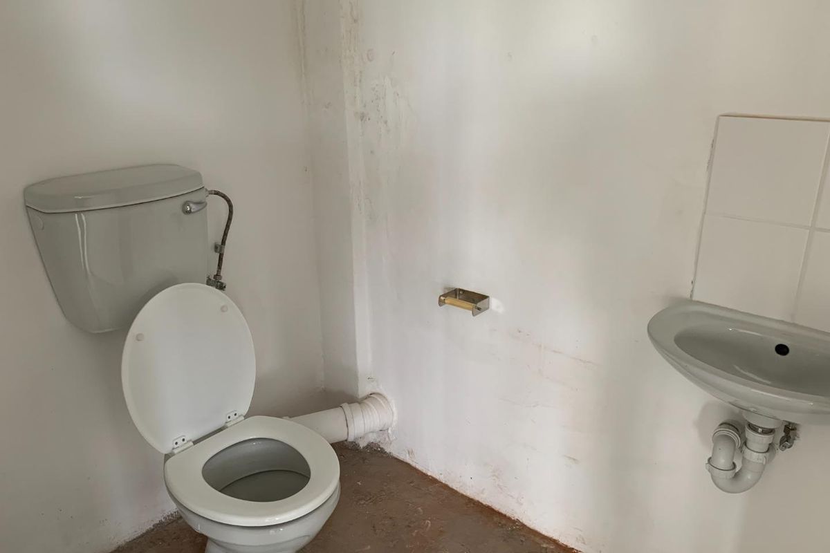 A basic, unfinished bathroom featuring a standard toilet and wall-mounted basin, requiring cosmetic updates and floor finishing.