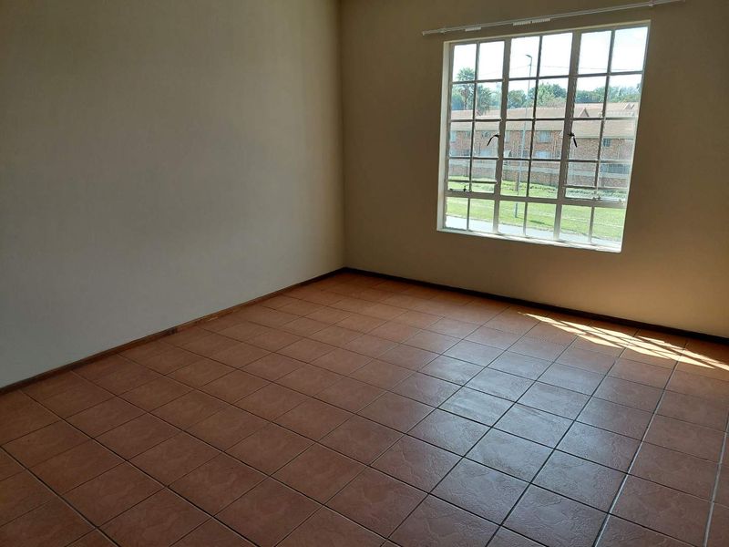 A bright, empty bedroom featuring neutral walls, ceramic floor tiles, and a large grid-pattern window providing natural light.