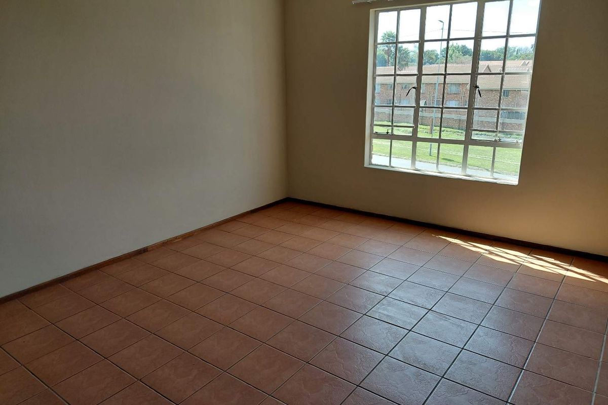 A bright, empty bedroom featuring neutral walls, ceramic floor tiles, and a large grid-pattern window providing natural light.