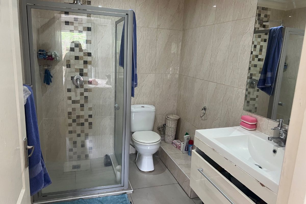 A functional bathroom featuring a glass shower enclosure, a vanity unit with basin, and neutral wall tiling with decorative mosaic accents.