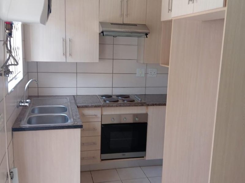 Compact kitchen featuring light wood-look cabinetry, built-in oven and hob, stainless steel sink, and neutral tiled flooring.