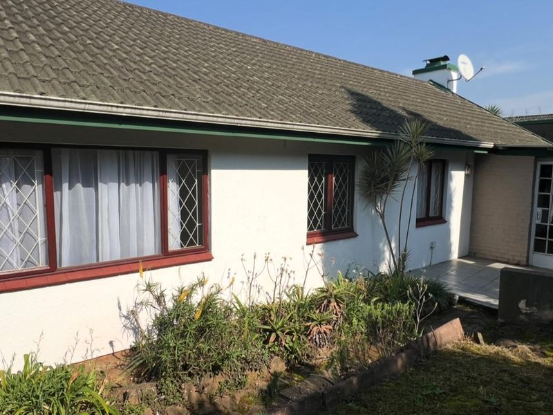 Rear exterior view of the townhouse featuring a tiled roof, leaded glass windows, and a paved patio area with established garden beds.