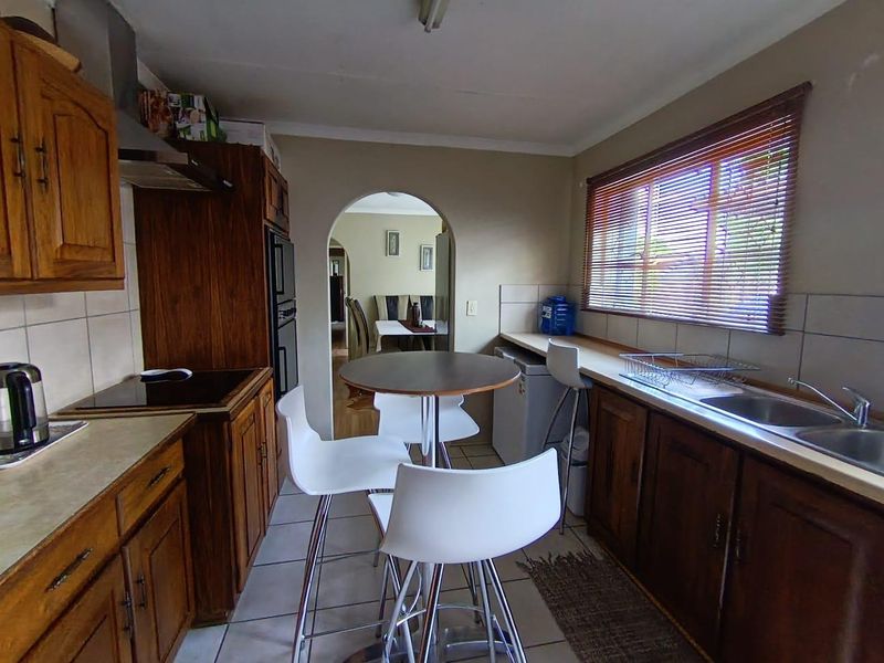 A functional kitchen featuring wooden cabinetry, built-in oven, electric hob, and a double stainless steel sink, with an archway leading to the dining area.