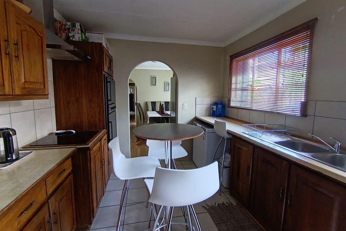 A functional kitchen featuring wooden cabinetry, built-in oven, electric hob, and a double stainless steel sink, with an archway leading to the dining area.