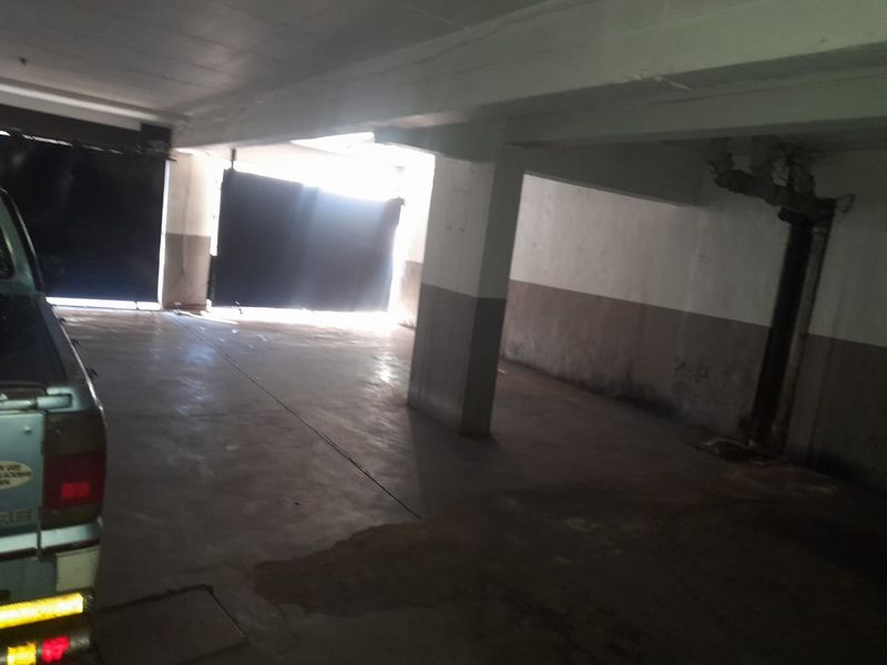 A functional, open-plan basement garage area featuring concrete flooring, structural support columns, and exposed utility piping.