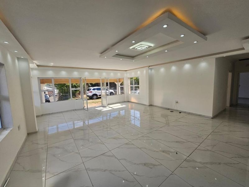 A spacious, bright, and empty living area featuring modern marble-look floor tiles, a sophisticated coffered ceiling with recessed lighting, and large aluminium-framed windows.