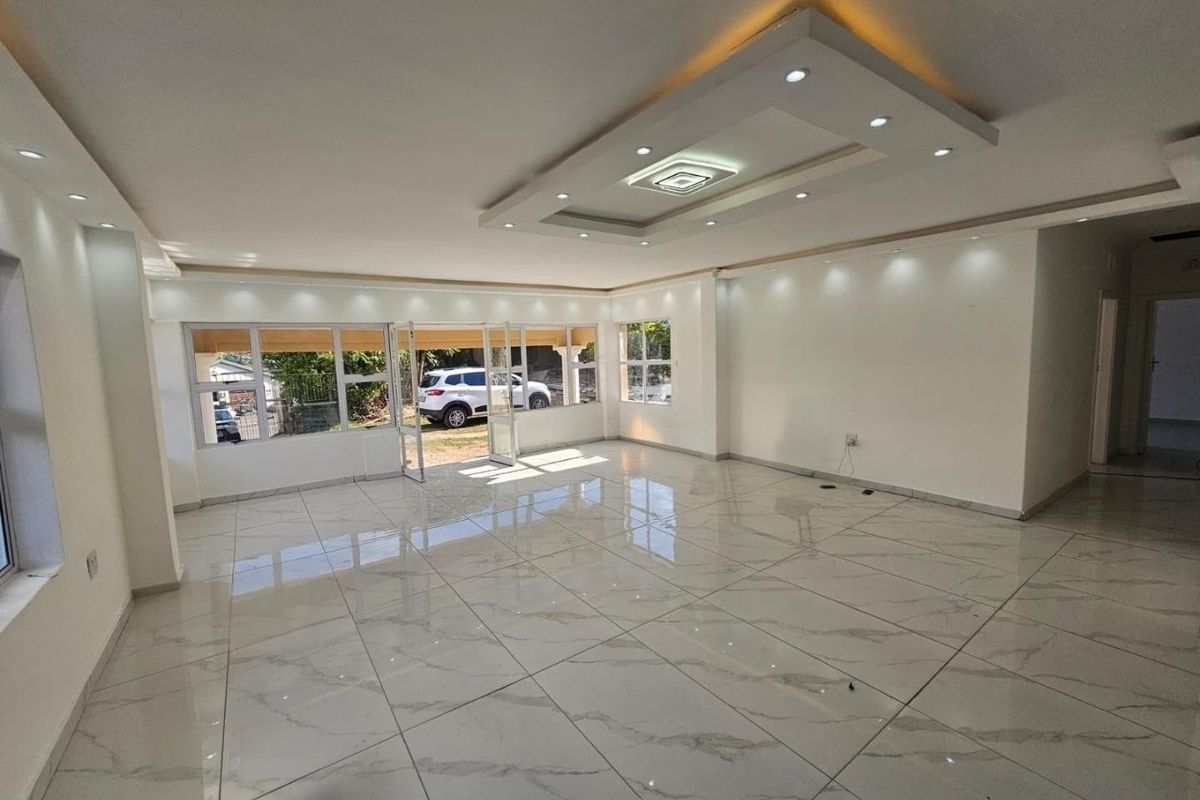 A spacious, bright, and empty living area featuring modern marble-look floor tiles, a sophisticated coffered ceiling with recessed lighting, and large aluminium-framed windows.