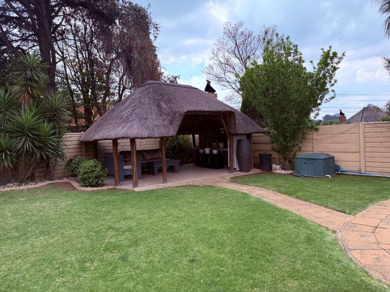 Outdoor thatched lapa area featuring a built-in braai, paved flooring, and a well-maintained garden setting, ideal for outdoor entertaining.