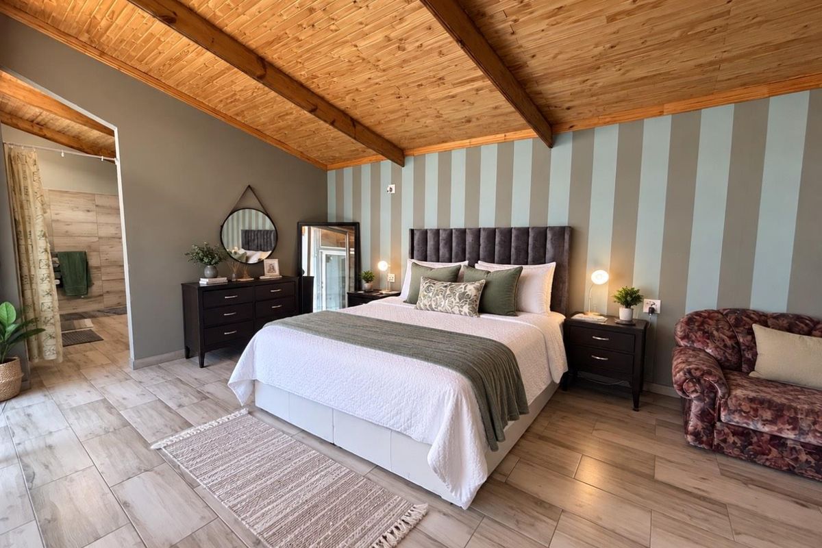 Spacious bedroom featuring a vaulted timber ceiling, wood-look tile flooring, and a striped feature wall with direct access to an en-suite bathroom.