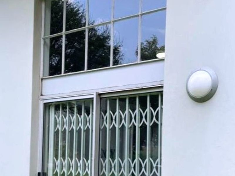 Exterior view of an apartment entrance featuring a sliding glass door with a security gate and a transom window above.