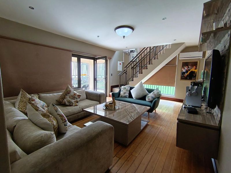 A well-maintained living room featuring hardwood flooring, a stone feature wall, and a staircase with metal railings, leading out to a patio area.