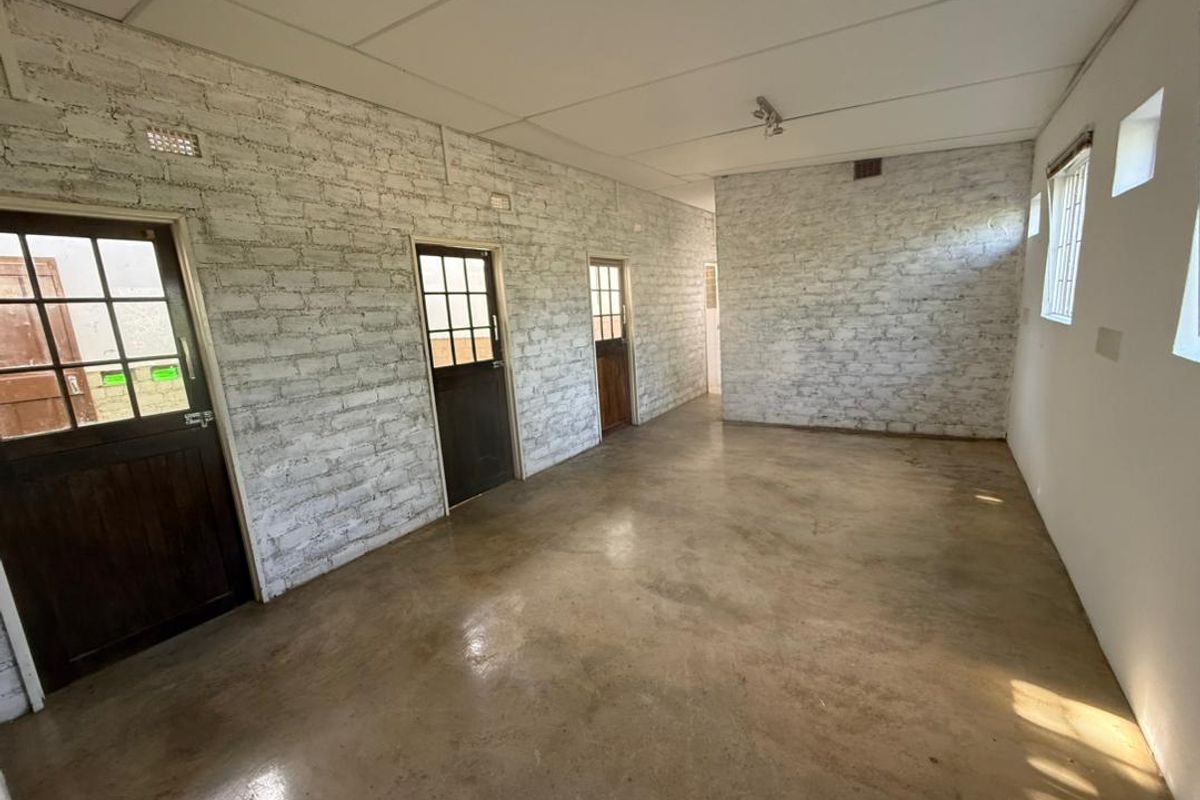 An empty, versatile interior space featuring exposed white-painted brick walls, polished concrete flooring, and multiple timber-framed access doors.