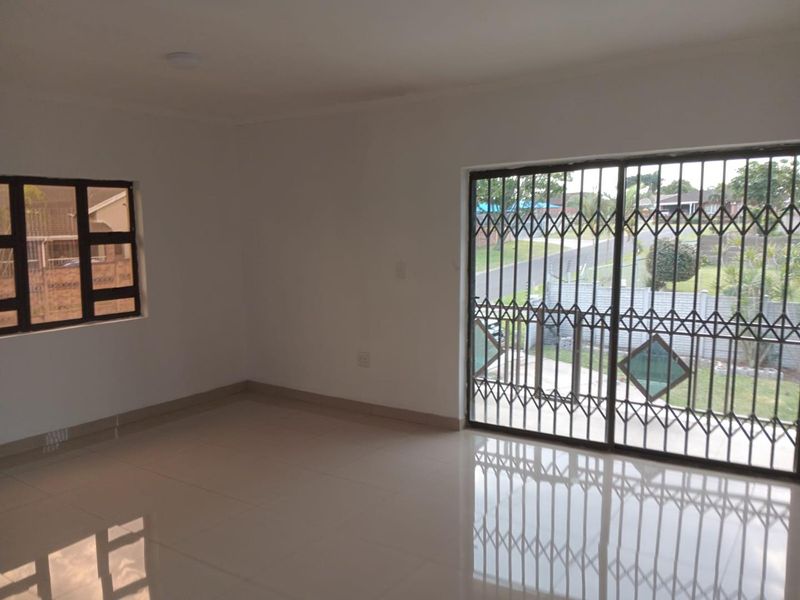A bright, empty living room featuring neutral tiled flooring, a sliding glass door with security gate, and a window with security bars.