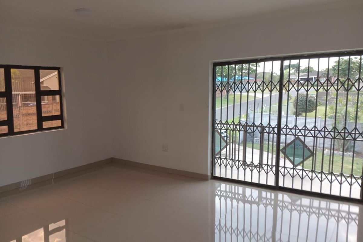 A bright, empty living room featuring neutral tiled flooring, a sliding glass door with security gate, and a window with security bars.