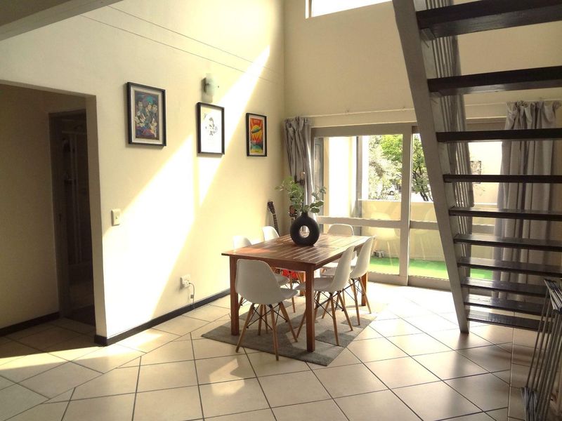 Open-plan living and dining area featuring high ceilings, tiled flooring, and a staircase leading to the upper level with access to a balcony.
