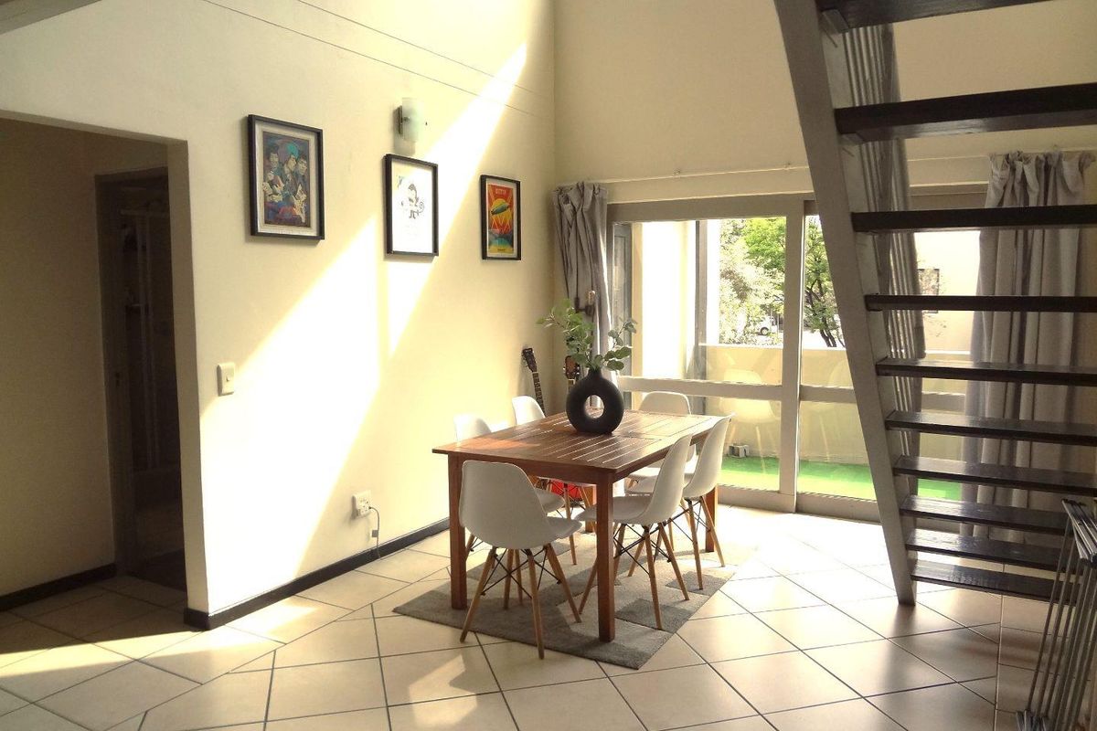 Open-plan living and dining area featuring high ceilings, tiled flooring, and a staircase leading to the upper level with access to a balcony.