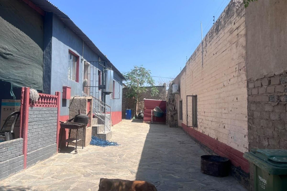 A rear exterior courtyard featuring stone paving, boundary walls with electric fencing, and an external water heater installation.