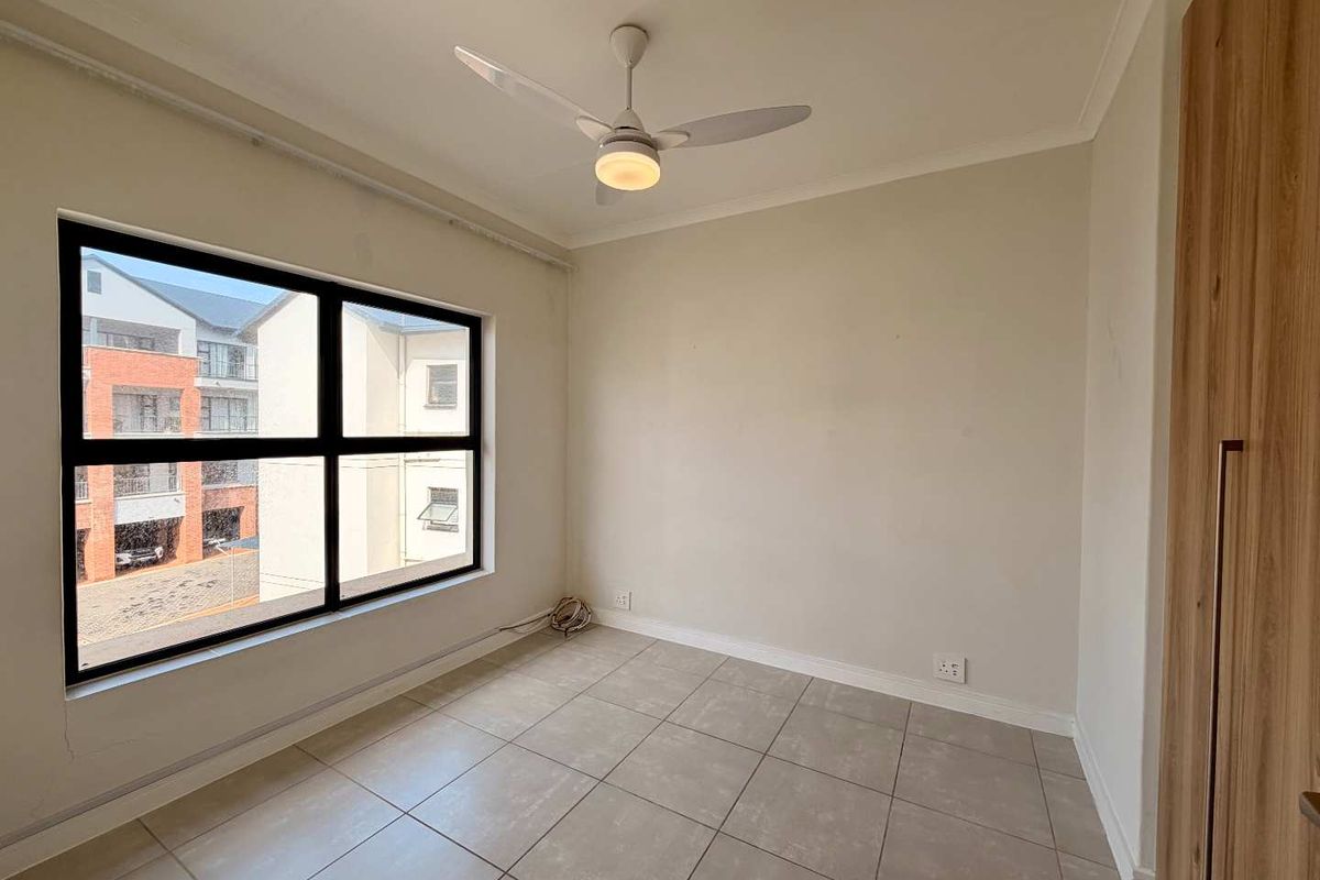 A bright, empty bedroom featuring neutral tiled flooring, a modern ceiling fan, and a built-in wardrobe with wood-grain finish.