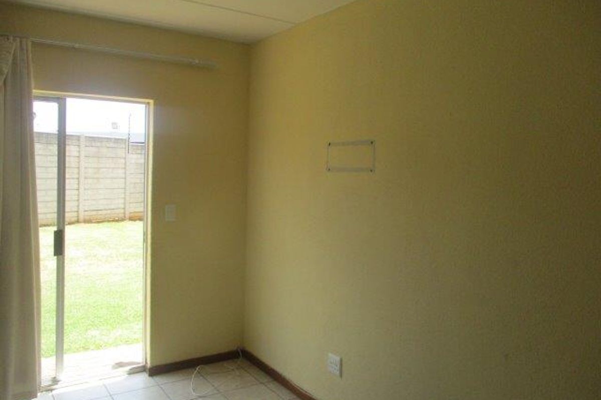 A simple bedroom featuring tiled flooring and a sliding glass door providing direct access to the rear garden area.