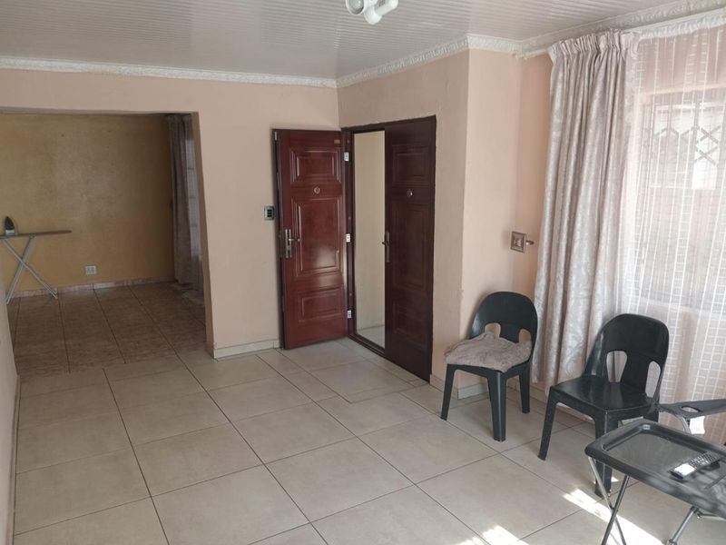 A vacant living area featuring tiled flooring, double entrance doors, and a beaded ceiling, offering a blank canvas for potential interior updates.
