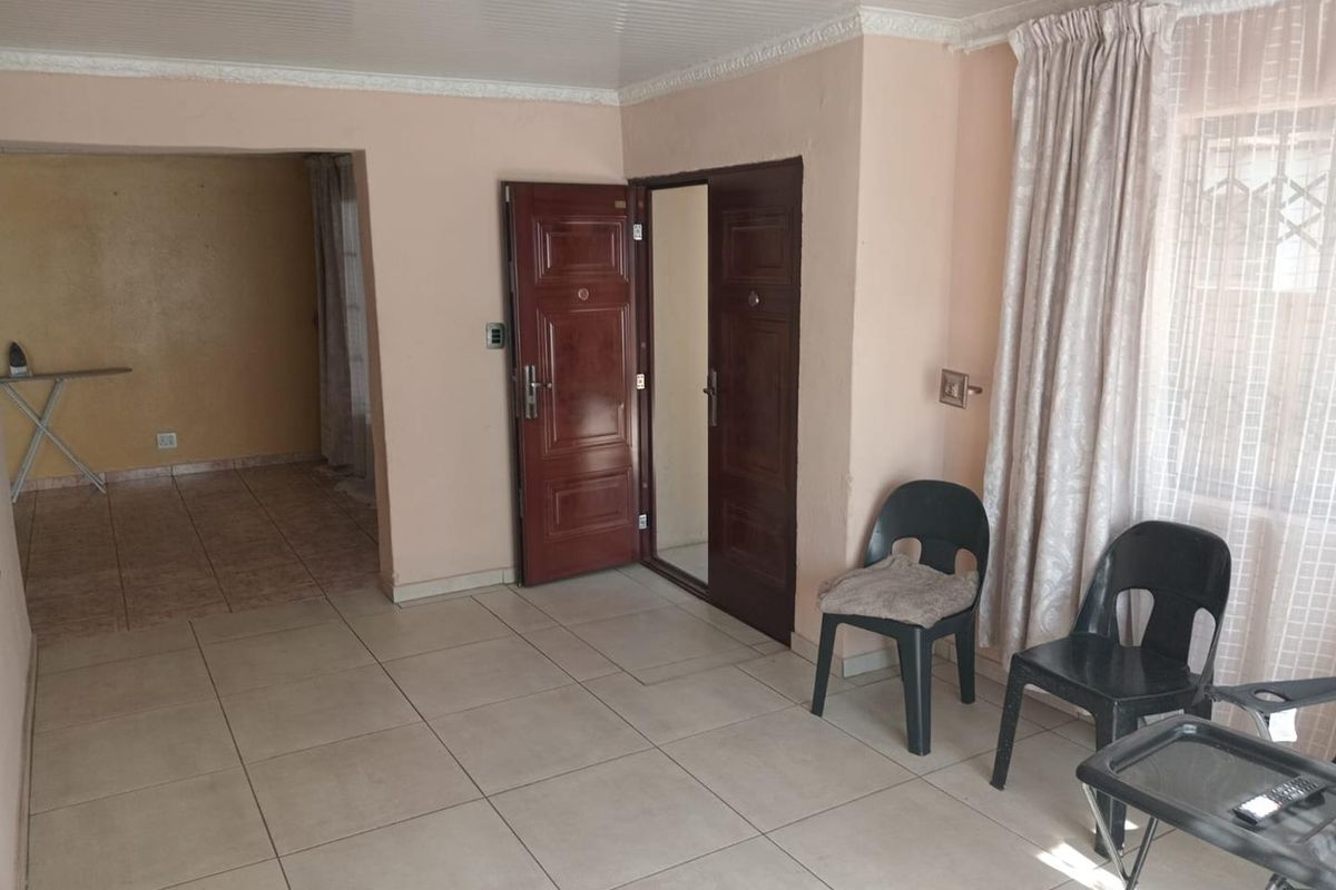 A vacant living area featuring tiled flooring, double entrance doors, and a beaded ceiling, offering a blank canvas for potential interior updates.