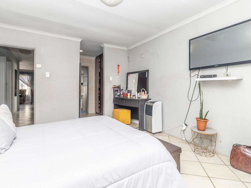 A bedroom featuring tiled flooring and built-in cupboards, with access to an adjoining room and bathroom area.