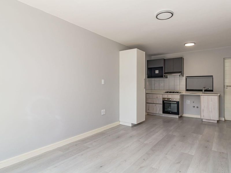 Modern open-plan living area featuring light laminate flooring, recessed lighting, and a compact kitchen equipped with a built-in oven, gas hob, and extractor fan.