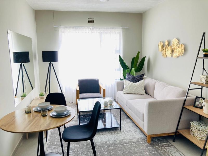A well-lit open-plan living and dining area featuring neutral wall tones, a large window, and a wall-mounted mirror.