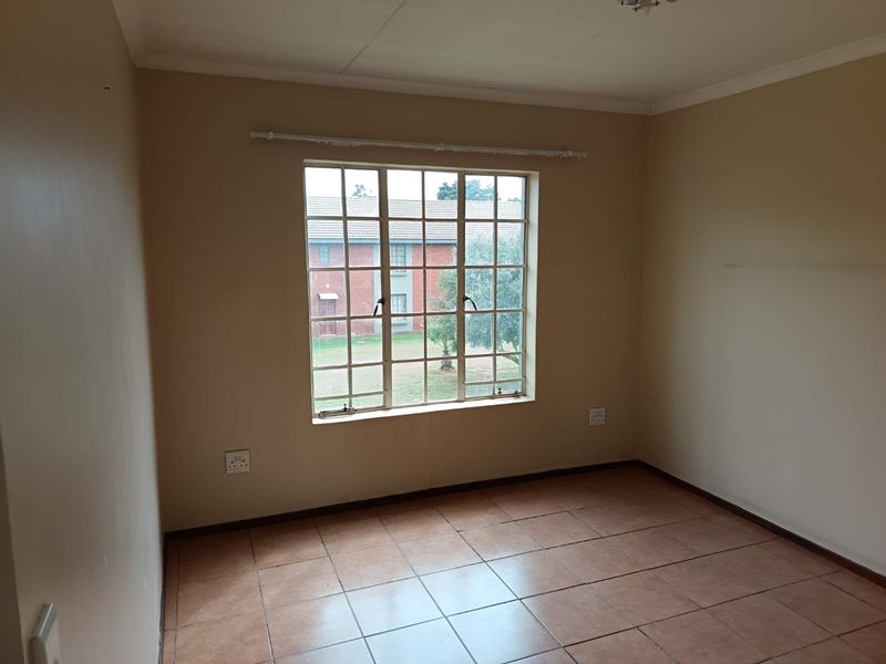 An empty bedroom featuring tiled flooring, a grid-pattern window with a curtain rail, and neutral wall paint.
