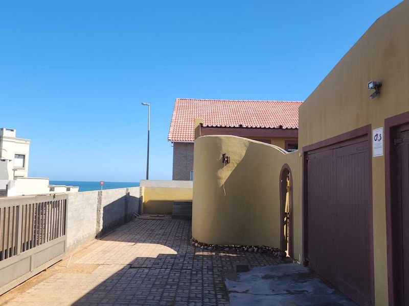 Exterior view of the property driveway featuring garage access, paved surfacing, and boundary walling with a glimpse of the ocean in the distance.