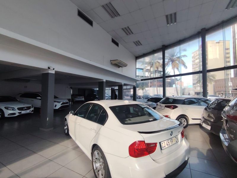 Spacious retail showroom featuring large floor-to-ceiling glass windows, tiled flooring, recessed lighting, and structural support columns, ideal for vehicle display.