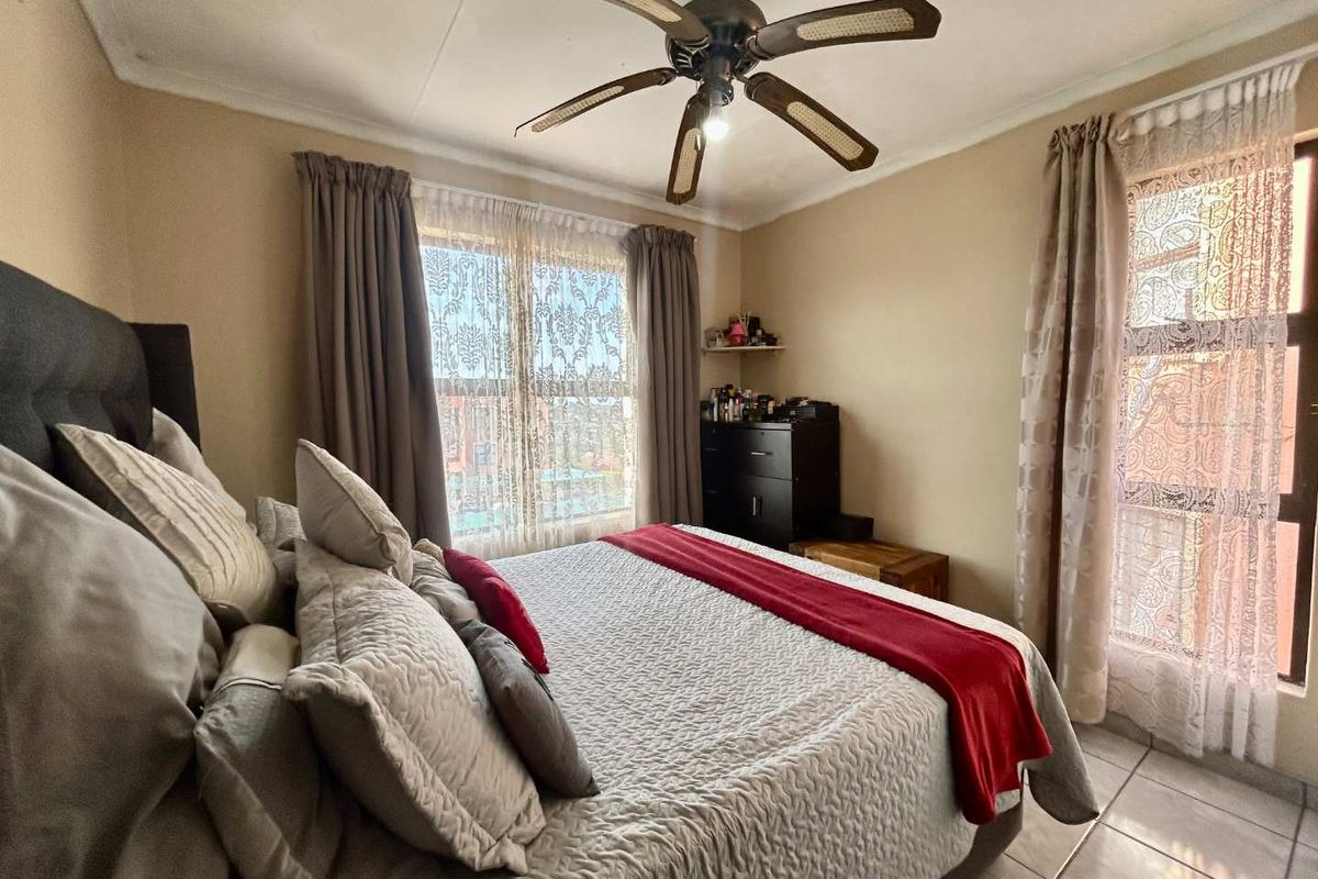 A well-lit bedroom featuring tiled flooring, a ceiling fan, and dual windows with natural light.