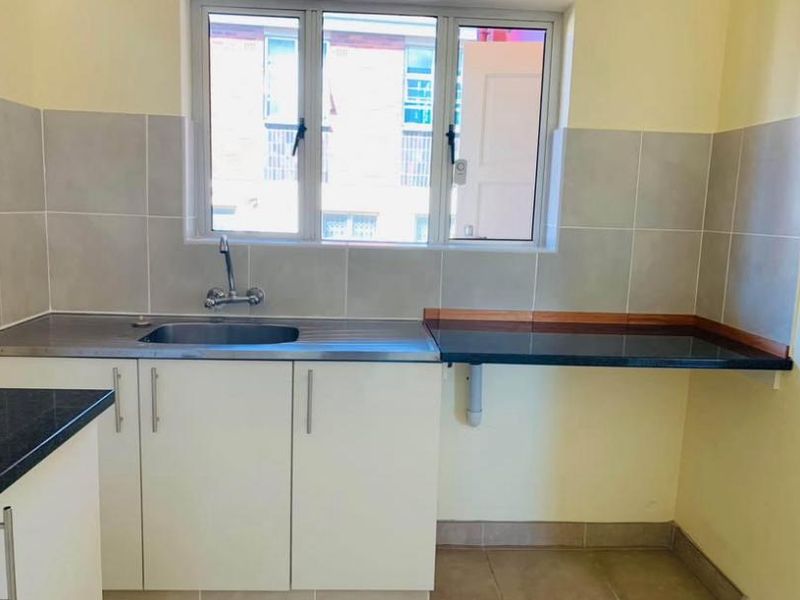 A functional kitchen area featuring a stainless steel sink, tiled splashbacks, and built-in cabinetry with dark countertops.