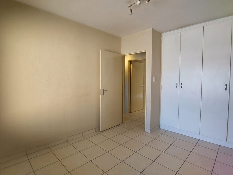 A clean, empty bedroom featuring neutral tiled flooring and ample built-in cupboard storage space.