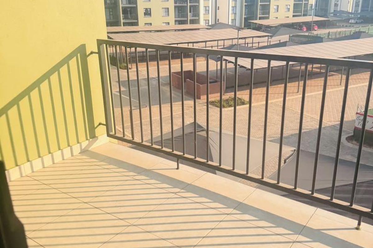 A clean, tiled balcony featuring a metal balustrade, offering an elevated view of the apartment complex parking area and surrounding buildings.